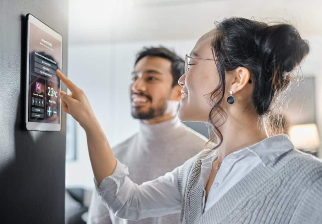 Woman and man smiling and looking at a tablet on the wall of their apartment